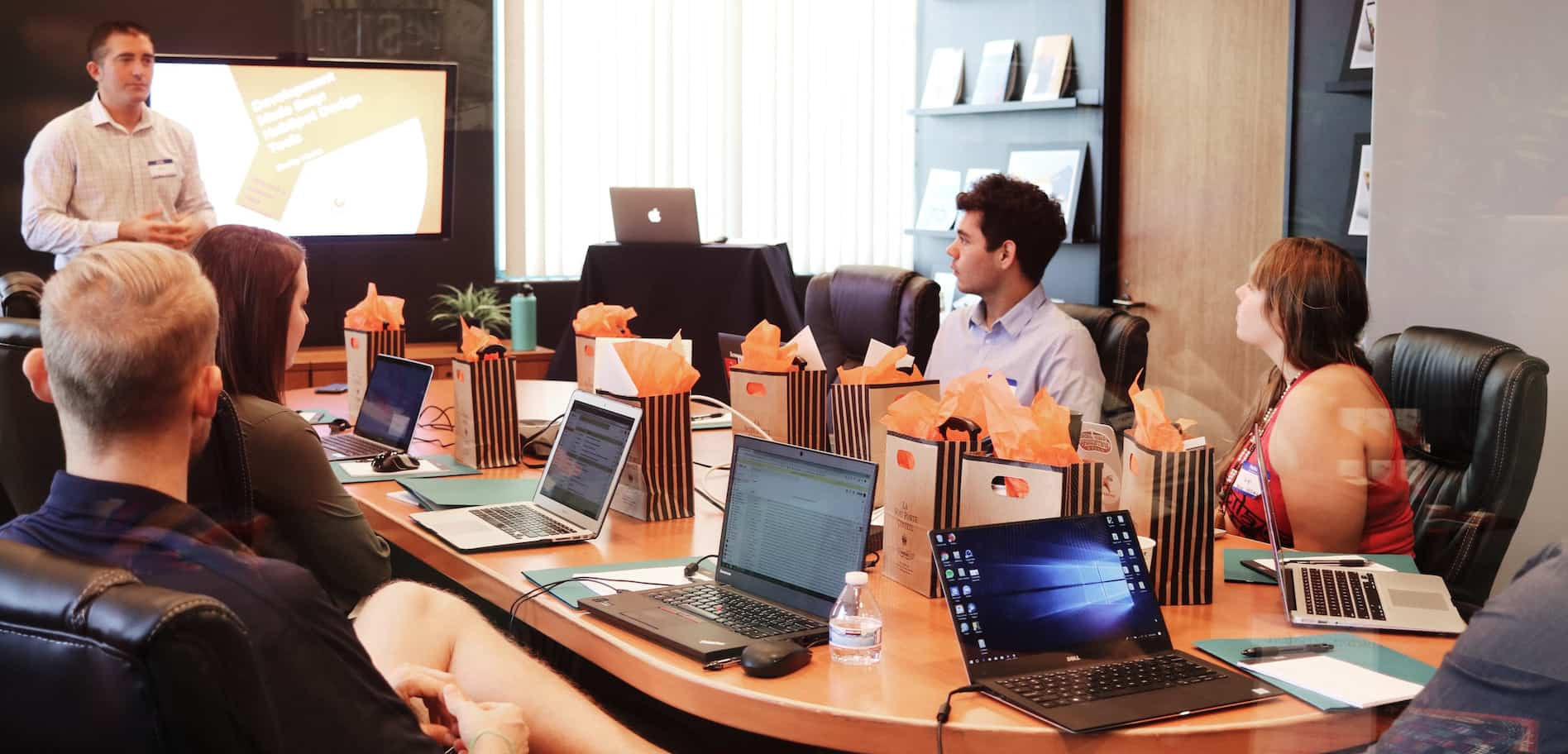 Person is showing image on the screen in front of the people behind the table