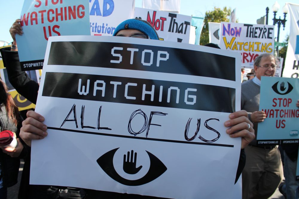 People are protesting. Holding banners with the sign: Stop watching all of us